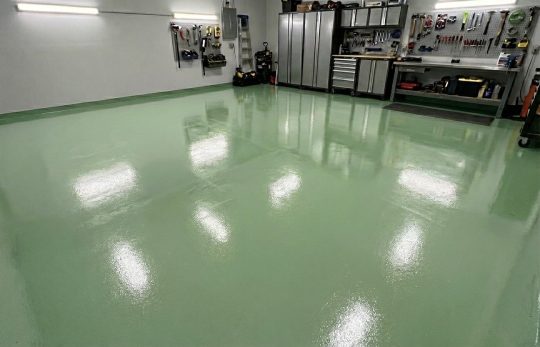 Lśniąca, gładka podłoga w kolorze RAL 6011 (zieleń mchu) zajmuje większą część kadru, odbijając światła sufitowe.