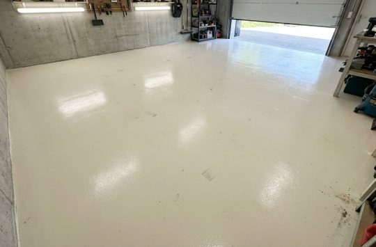 Jasna, błyszcząca posadzka w kolorze RAL 7032 pokrywa całe wnętrze garażu.